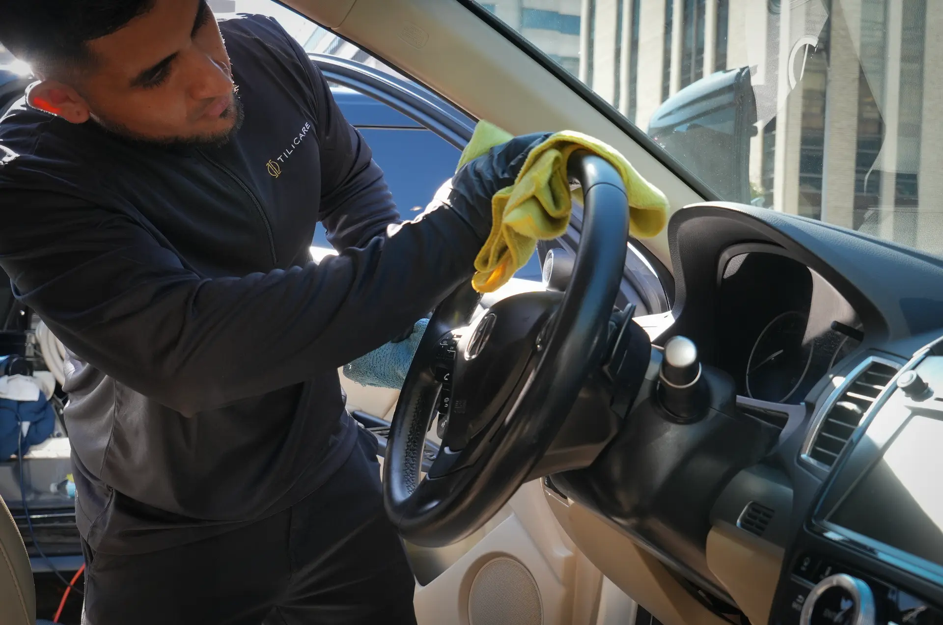 Tilicare detailer hand-cleaning a steering wheel with a microfiber cloth
