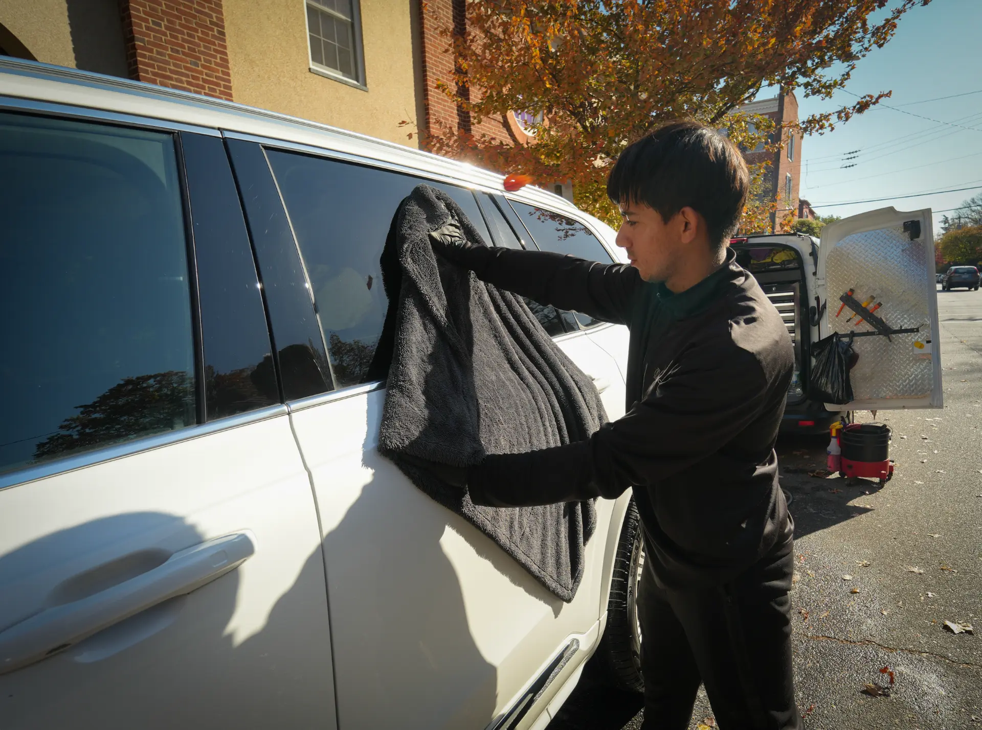 Tilicare detailer drying a white SUV with a gray towel beside the Tilicare van
